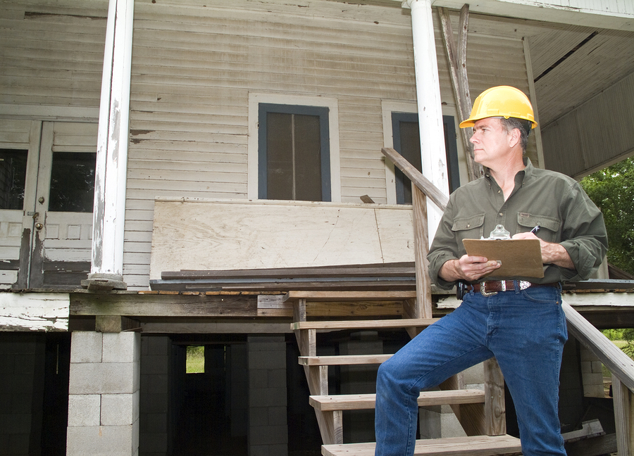 man in a hard hat holding a clipboard standing on the steps of an old rundown house